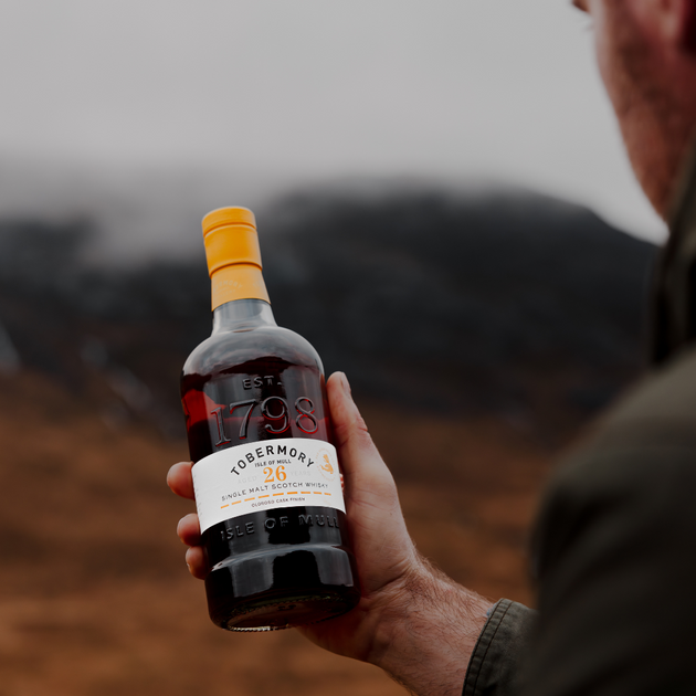 Man Holding Hebridean Series 26 Year Old Bottle with Mountain Backdrop